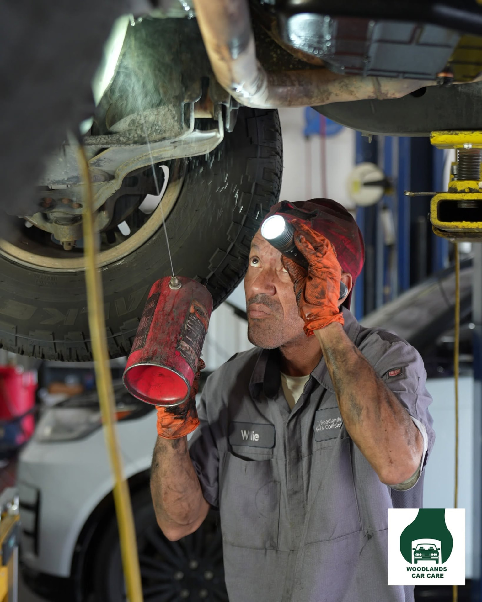 Woodlands Car Care technician inspecting a vehicle underbody with a work light
